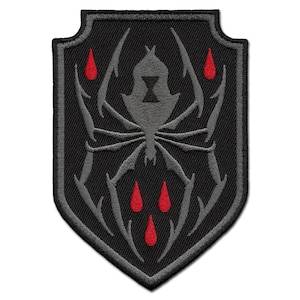 May include: A black embroidered patch in a shield shape. The design features a grey spider with a black hourglass on its back, surrounded by grey spider legs. Red teardrops are below the spider.
