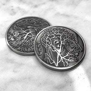 May include: Two silver-toned metal coins with intricate designs. One coin features a tree-like pattern with the word "SHADOW" inscribed, while the other coin depicts a detailed anatomical illustration of a human head with the word "SELF" inscribed.
