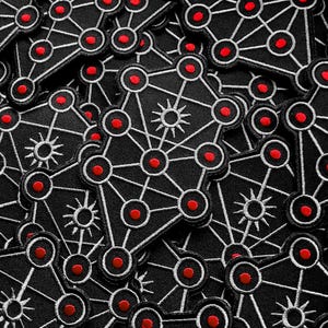 May include: A collection of black patches with a white geometric design featuring red circles and starbursts. The patches are densely packed together, creating a repeating pattern. The patches are likely iron-on or sew-on.