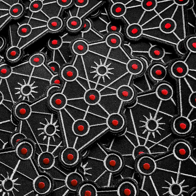 May include: A collection of black patches with a white geometric design featuring red circles and starbursts. The patches are densely packed together, creating a repeating pattern. The patches are likely iron-on or sew-on.