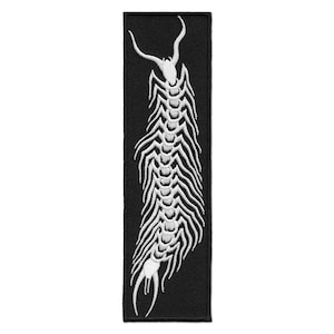 May include: A black rectangular patch with a white embroidered design of a centipede-like creature. The design features a head with curved horns and a segmented body with many legs. Suitable for application on clothing or accessories.