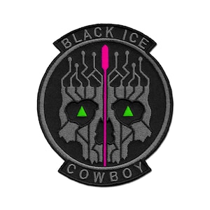 May include: Black and grey embroidered patch featuring a skull design. The skull has green triangle eyes and a pink vertical line down the centre. The text "BLACK ICE COWBOY" is around the outside of the patch.