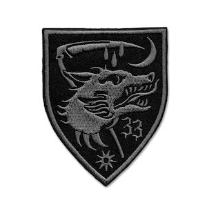 Op de afbeelding: Zwarte en grijze geborduurde patch met een wolvenkop met een halve maan en druppels bloed erboven. Het nummer "33" staat onder de wolvenkop en een ster bevindt zich onderaan de patch.