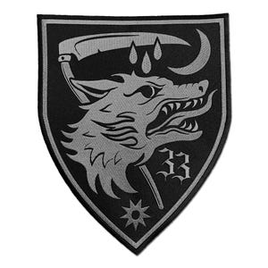 May include: A black and grey patch featuring a wolf's head, a scythe, and the number 33. The wolf has sharp teeth and is set against a shield shape. A crescent moon and star are also included in the design.