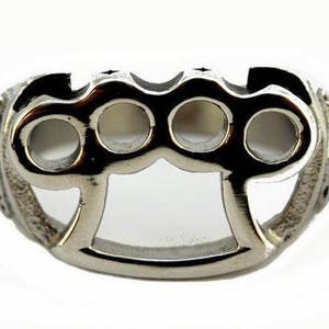 May include: A silver metal ring with a knuckle duster design. The ring has four holes in the knuckle duster portion.