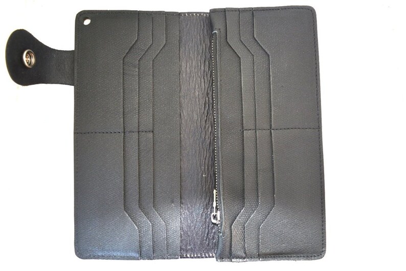 Puede incluir: Una cartera de cuero negro con m&uacute;ltiples ranuras para tarjetas y un compartimento con cremallera. La cartera tiene un cierre de solapa con un bot&oacute;n.