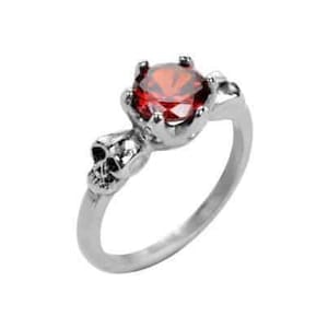Op de afbeelding: Een zilveren ring met een rode edelsteen en twee schedeldetails op de band.