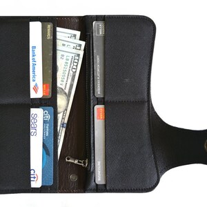 Puede incluir: Una cartera de cuero negro con cierre de solapa y asa de correa. La cartera est&aacute; abierta y muestra varias tarjetas de cr&eacute;dito y efectivo en su interior.