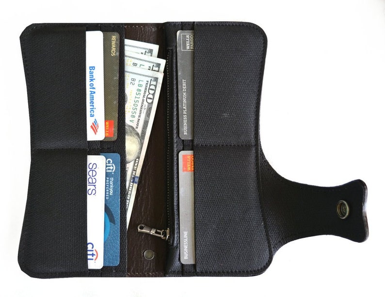 Puede incluir: Una cartera de cuero negro con cierre de solapa y asa de correa. La cartera est&aacute; abierta y muestra varias tarjetas de cr&eacute;dito y efectivo en su interior.