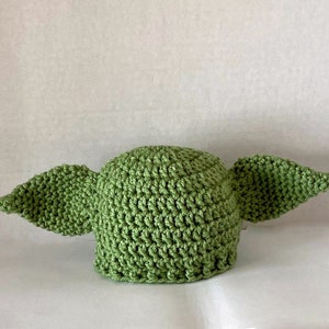 May include: Green crocheted hat with two large ears, resembling a popular fictional character.
