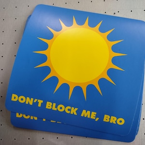 Puede incluir: Un sol azul y amarillo con rayos y el texto "DON'T BLOCK ME, BRO" sobre un fondo azul.