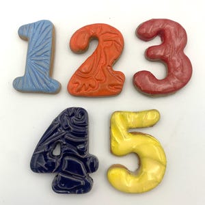 May include: Five ceramic number tiles in different colors. The numbers are 1, 2, 3, 4, and 5. The tiles are decorated with different patterns.