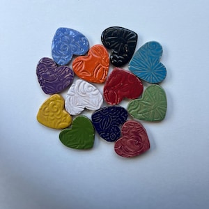May include: A collection of 12 ceramic heart-shaped tiles with various patterns and colors, including purple, red, blue, green, yellow, and white.