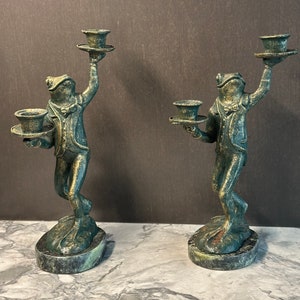 May include: A pair of green frog candle holders with a vintage look. Each frog is holding a tray with a candle holder on top. The frogs are standing on a round green base.