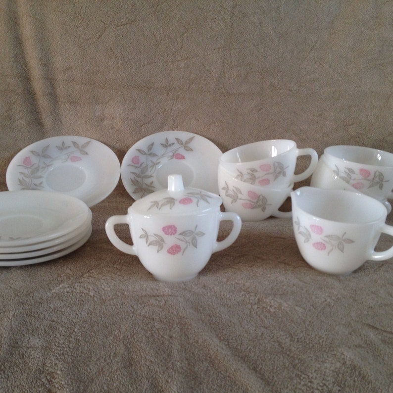 May include: A white tea set with a pink and grey floral design. The set includes a creamer and sugar bowl, four cups, and four saucers.