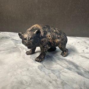 May include: A black and brown bear figurine with a textured surface. The bear is standing on a white marble surface.