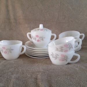 May include: A set of white milk glass teacups and saucers with a pink and grey floral design. The set includes a creamer and sugar bowl with lids.
