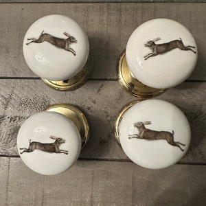 May include: Four white ceramic door knobs with a gold base. Each knob features a brown rabbit running across the front.