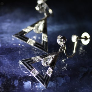 May include: A pair of silver triangle earrings with black enamel accents and clear rhinestones.