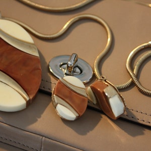 May include: A gold chain necklace with three oval-shaped pendants. The pendants are made of brown, white, and gold-colored resin.