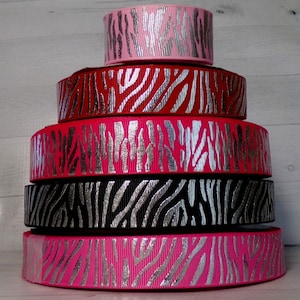 May include: Stack of five zebra print ribbon rolls with silver glitter accents. The ribbons are pink, red, black, and pink.