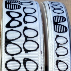 May include: Two white ribbon spools with black and white printed designs of glasses and sunglasses. The ribbon is white with black printed designs.