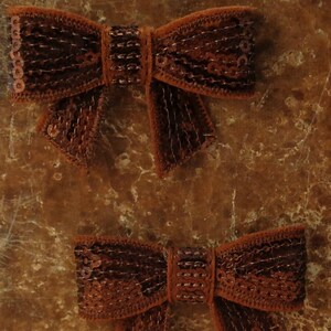 May include: Two brown velvet bows with sequins. The bows are tied in a knot and have a pointed end.