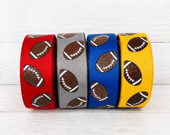 May include: Four spools of grosgrain ribbon arranged in a row. Each spool features a repeating pattern of brown American footballs with white laces. The ribbons are colored red, light gray, royal blue, and yellow, respectively.