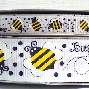 May include: White ribbon with a repeating pattern of black and yellow bees, black dots, and the text "Buzz Buzz" in black.