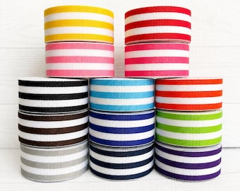 May include: A collection of twelve spools of grosgrain ribbon arranged in a stack. Each spool features horizontal stripes in various colours including yellow, red, pink, black, light blue, orange, brown, dark blue, lime green, grey, and purple.