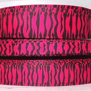 May include: Three spools of pink and black zebra print ribbon. The ribbon is a satin-like material with a slight sheen.