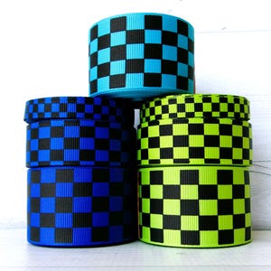 May include: A stack of colorful ribbon rolls with a checkerboard pattern. The rolls are in shades of blue, green, and black. The ribbon is likely used for crafting, gift wrapping, or other decorative purposes.