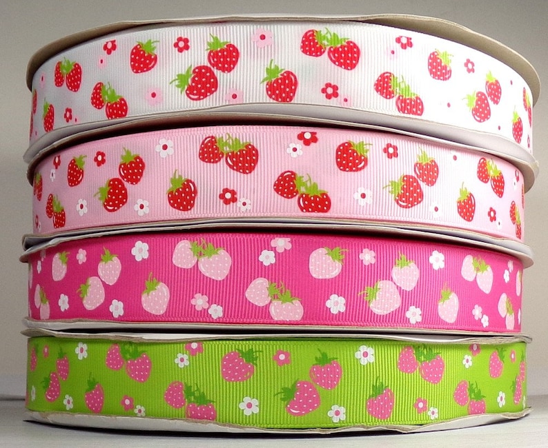 May include: Four rolls of ribbon with a strawberry print. The ribbon is pink, white, green, and pink. The strawberries are red with white seeds.
