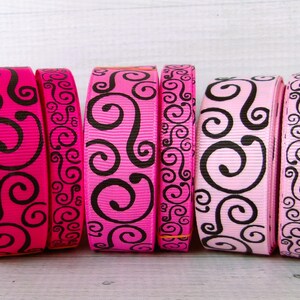 May include: Six rolls of decorative ribbon in shades of pink, ranging from hot pink to light pink. Each ribbon features a black, swirling scroll design. The ribbons are arranged side by side.