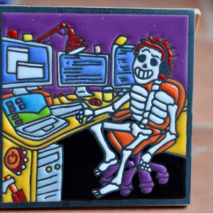 Op de afbeelding: Een kleurrijke keramische tegel met daarop een skelet dat aan een computerbureau zit. Het skelet draagt een koptelefoon en een feloranje shirt. Het bureau heeft een computermonitor, een toetsenbord en een lamp. De achtergrond is een paarse muur.
