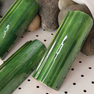 Puede incluir: Cuatro azulejos de cerámica verde con textura acanalada. Los azulejos están dispuestos en una fila y están rodeados de pequeñas piedras.