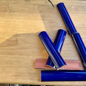 Puede incluir: Cuatro piezas de moldura de azulejos de cerámica azul con bordes redondeados. Los azulejos están dispuestos sobre una superficie de madera.