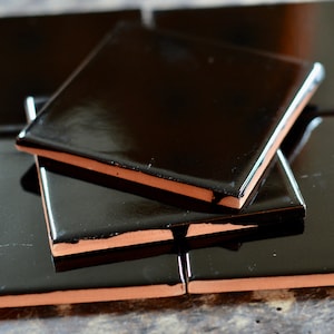 May include: A stack of black ceramic tiles with a glossy finish. The tiles have a slightly raised edge and are arranged in a staggered pattern.