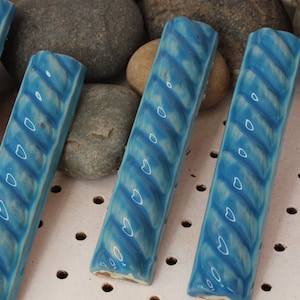 May include: Four blue ceramic tiles with a rope-like design and white accents. The tiles are arranged in a row on a white surface with small holes.