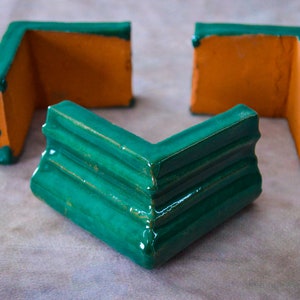 Puede incluir: Tres piezas de esquina de cerámica en verde y naranja. Las piezas de esquina están diseñadas para ser utilizadas como moldura para una pared u otra superficie.