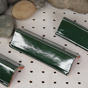 May include: Four green ceramic tile corner pieces with a glossy finish. The tiles are arranged in a row on a white surface with small holes.