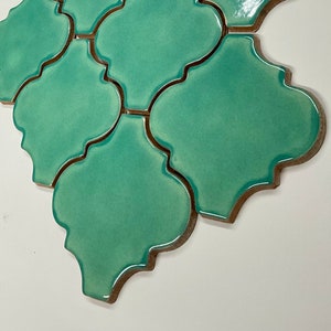 May include: A close-up of a group of green ceramic tiles with a decorative, scalloped edge. The tiles are arranged in a staggered pattern.