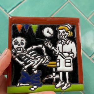 Può includere: Una piastrella di ceramica colorata che raffigura due scheletri, uno vestito da medico e l'altro da paziente. Il medico tiene una siringa e il paziente indossa jeans blu. La piastrella ha uno sfondo nero con accenti verdi, arancioni e gialli.