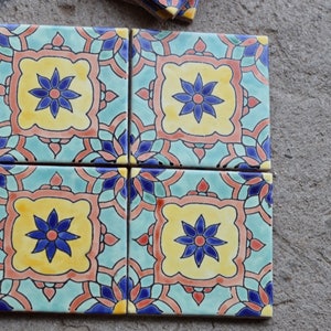 Peut inclure: Quatre carreaux de céramique carrés avec un motif floral coloré. Les carreaux présentent un schéma de couleurs bleu, jaune et orange avec un motif répétitif de fleur stylisée.