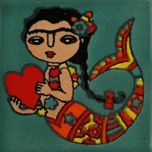 May include: A colorful ceramic tile featuring a mermaid with a red heart. The mermaid has black hair, a red and yellow striped top, and a colorful fishtail.