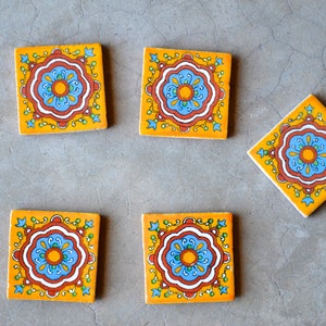 May include: Five square ceramic tiles with a yellow background and a blue, red and white floral design.