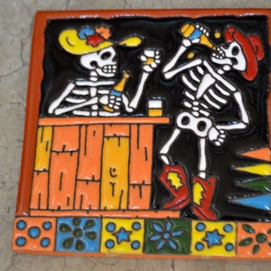 May include: Two skeleton figures in a bar setting, one holding a bottle and the other a glass, with a colorful tile design around the border.
