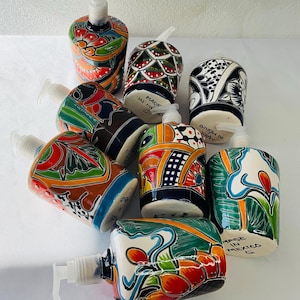 May include: A collection of eight colorful ceramic soap dispensers with intricate floral and geometric designs. Each dispenser features a unique pattern and vibrant colors, including blue, green, red, orange, yellow, and black. The dispensers are made in Mexico and have a traditional Mexican style.