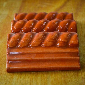 May include: Three terracotta tiles with a rope-like design. The tiles are a deep reddish-brown color and have a glossy finish.