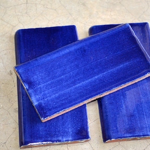 May include: Three blue ceramic tiles with a slightly textured surface. The tiles are rectangular and have rounded edges.